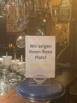 Restaurant Laterne in Berlin Schöneberg. Man sieht ein kleines Warnschild mit dem Text "Wir zeigen Ihnen Ihren Platz!", das auf der Theke steht. 